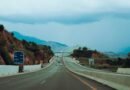 gray concrete road between brown and green mountains under blue sky