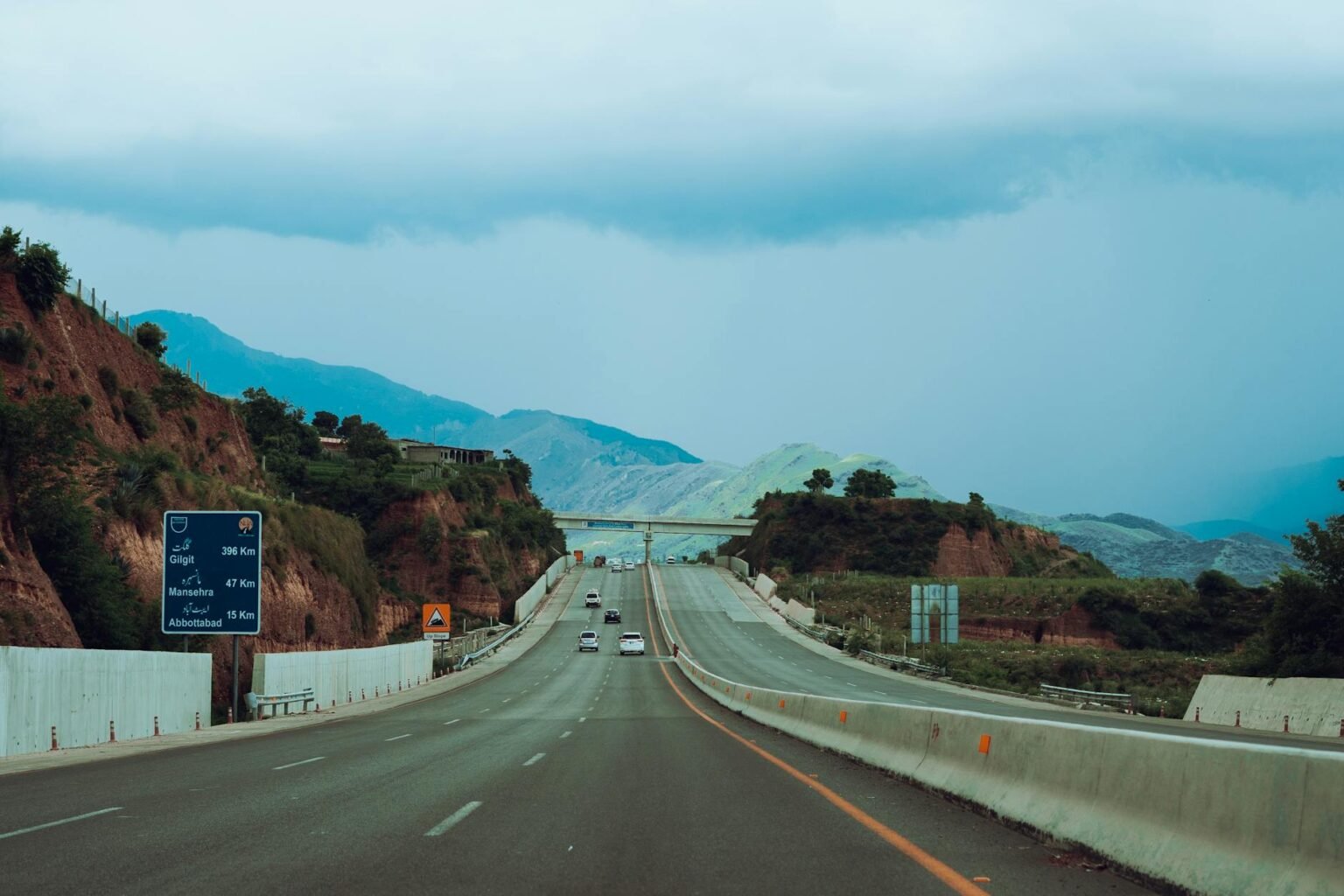gray concrete road between brown and green mountains under blue sky