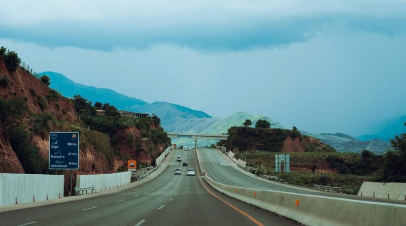gray concrete road between brown and green mountains under blue sky